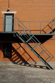 Metal staircase and shadow on a red brick wall exterior, creating a geometric pattern.