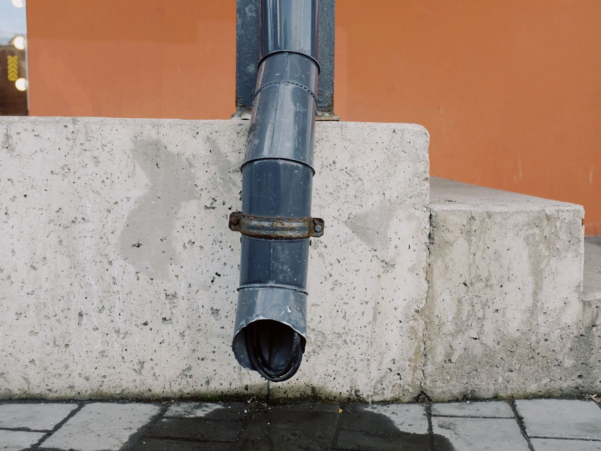 Old metal drain pipe on a concrete wall with water stains.