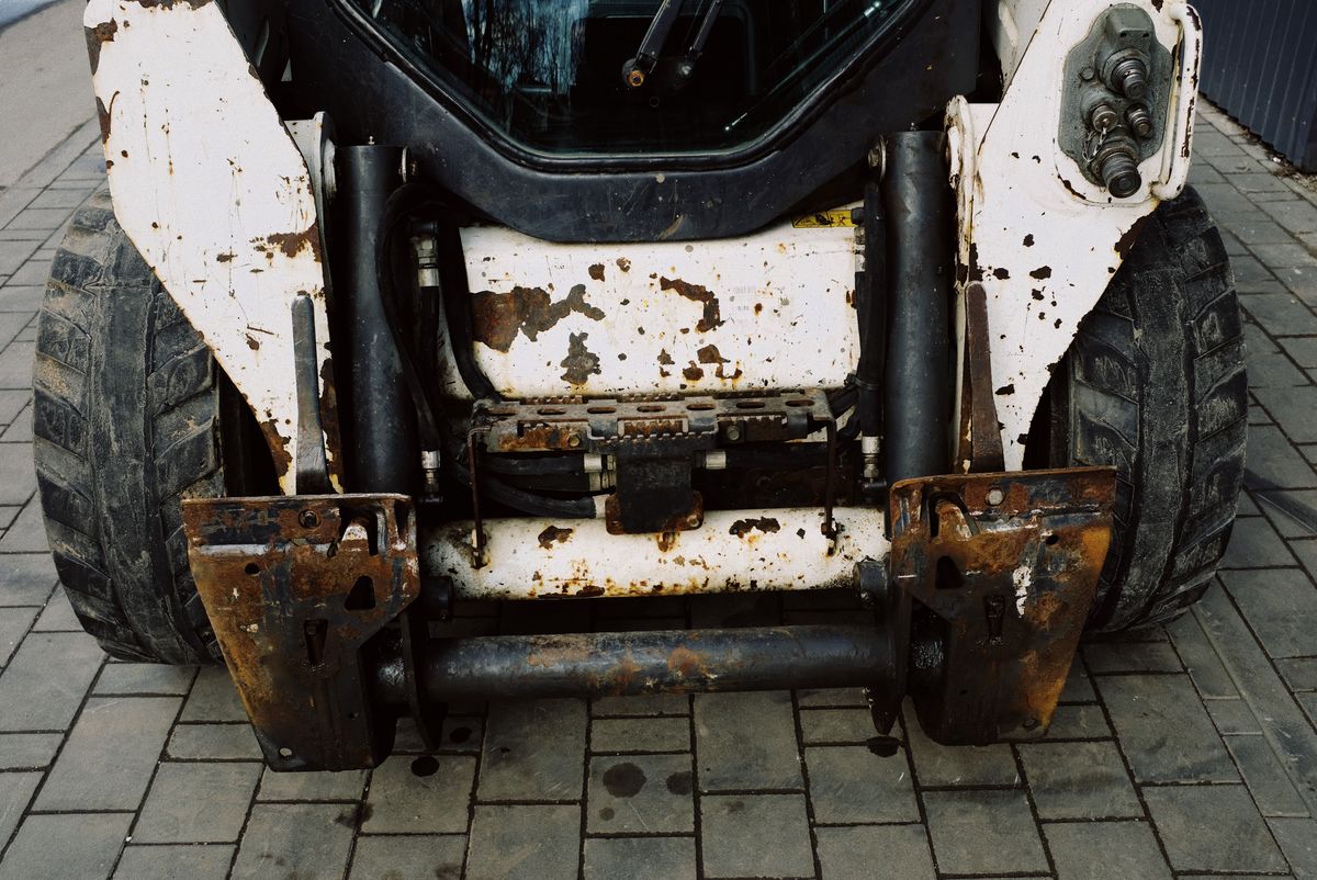 The rusted, worn rear of an old skid steer loader awaiting repair