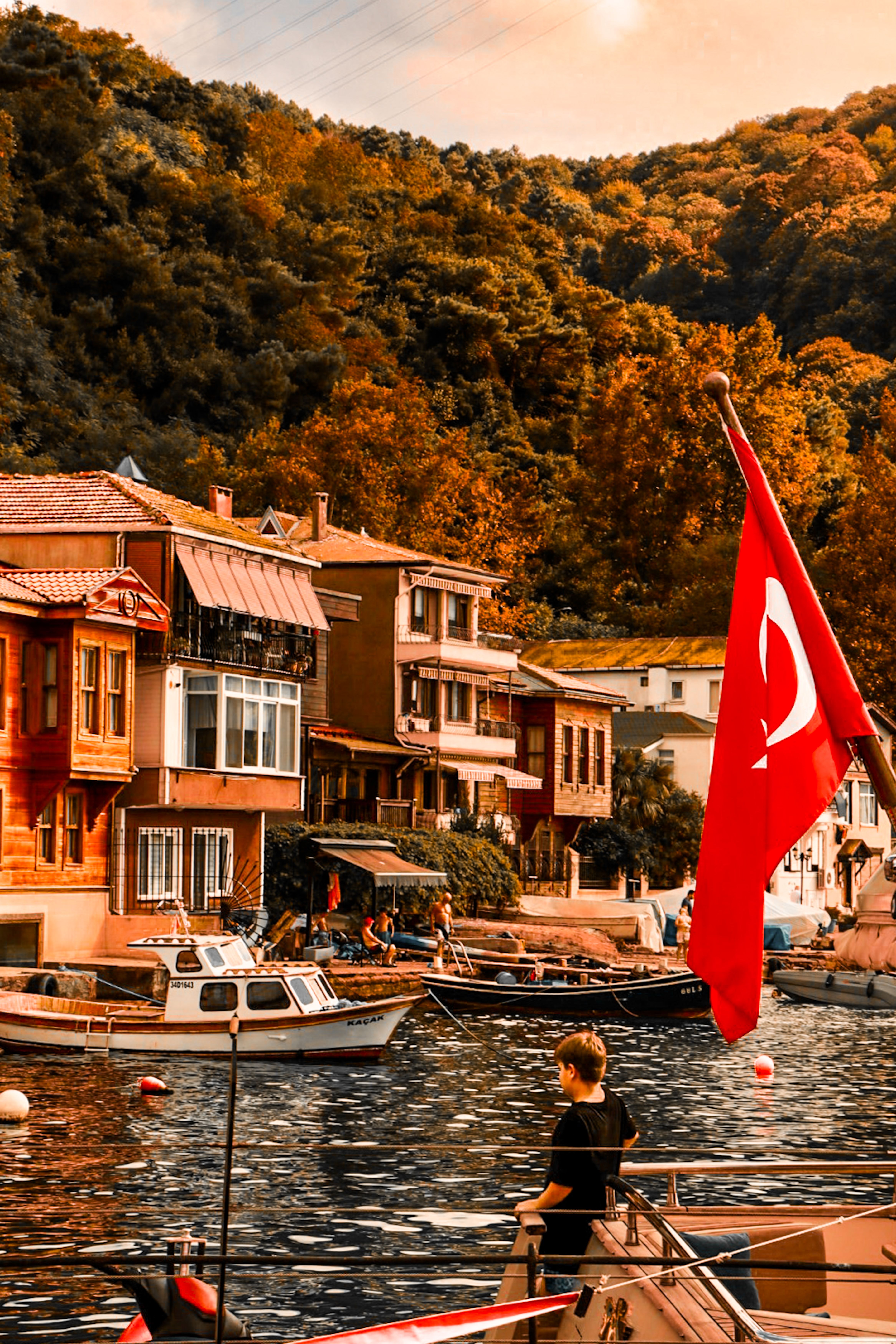 Picturesque waterfront in Anadolu Kavağı, İstanbul, with a Turkish flag and scenic boats.