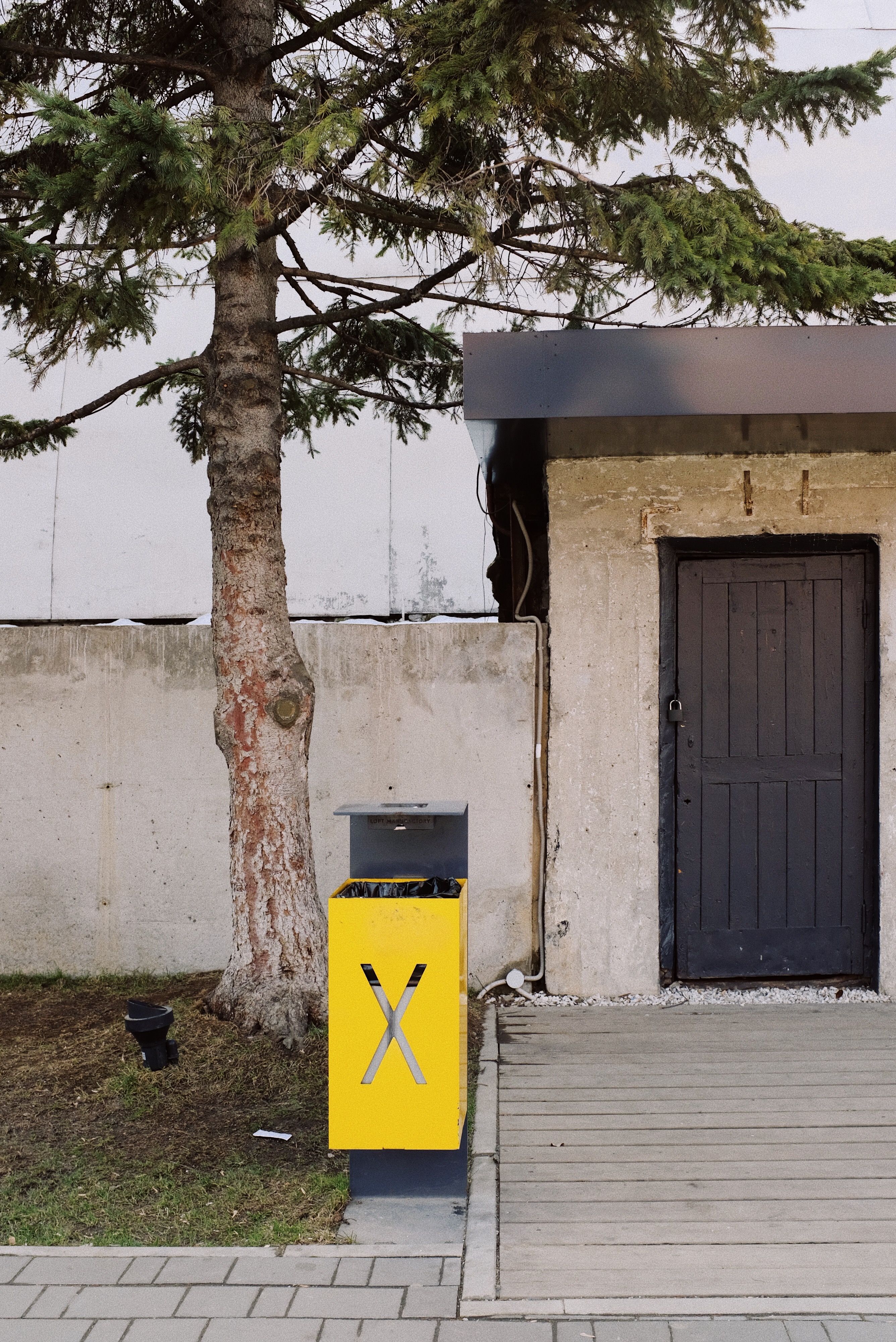 Vivid trash box in front of entrance to estate with black door and blind concrete fence
