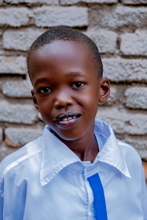 Free Cheerful young boy in a white shirt standing against a rustic brick wall. Stock Photo