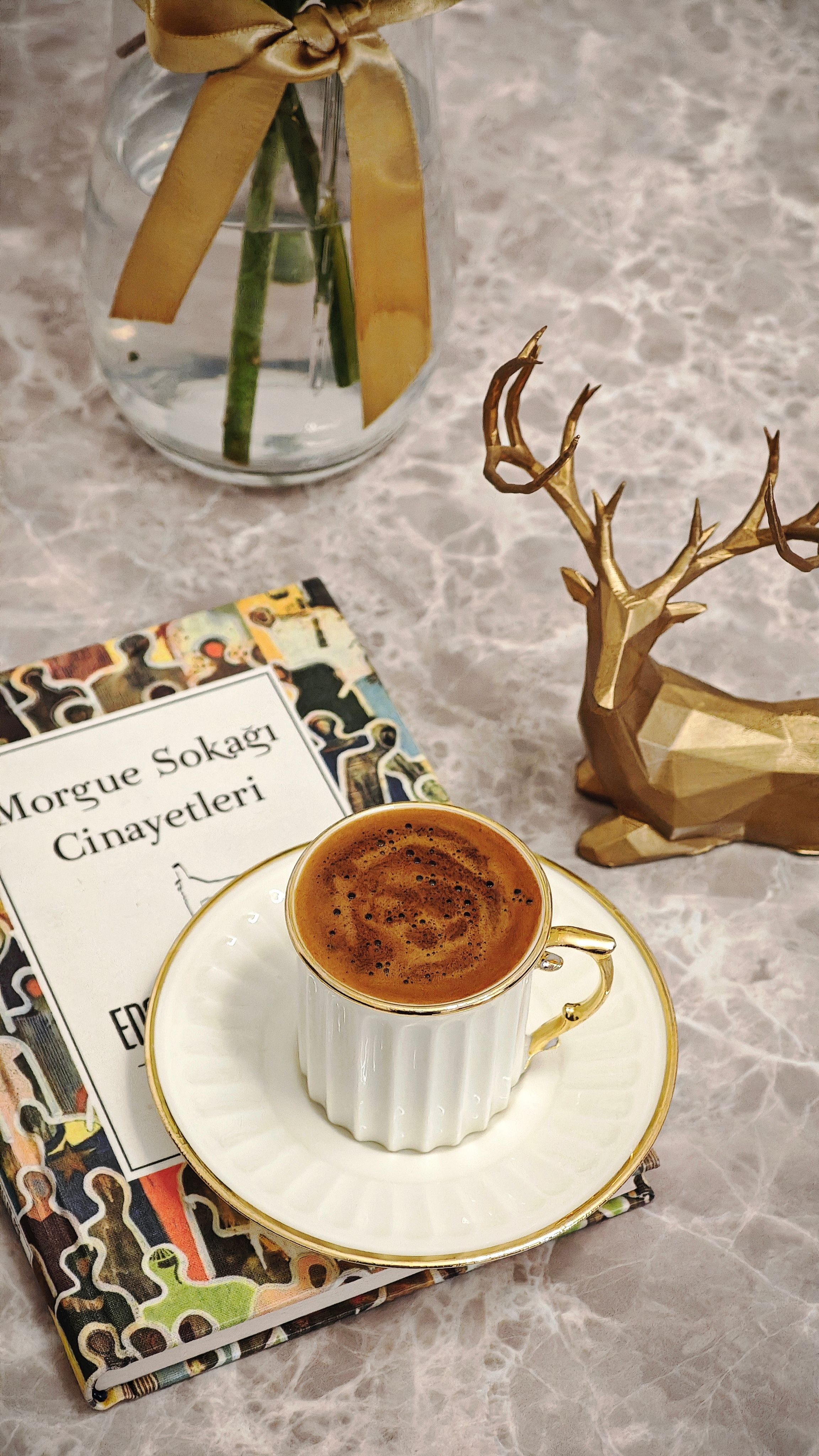 Stylish coffee cup on marble with a crime novel and gold deer sculpture, perfect for a cozy setting.