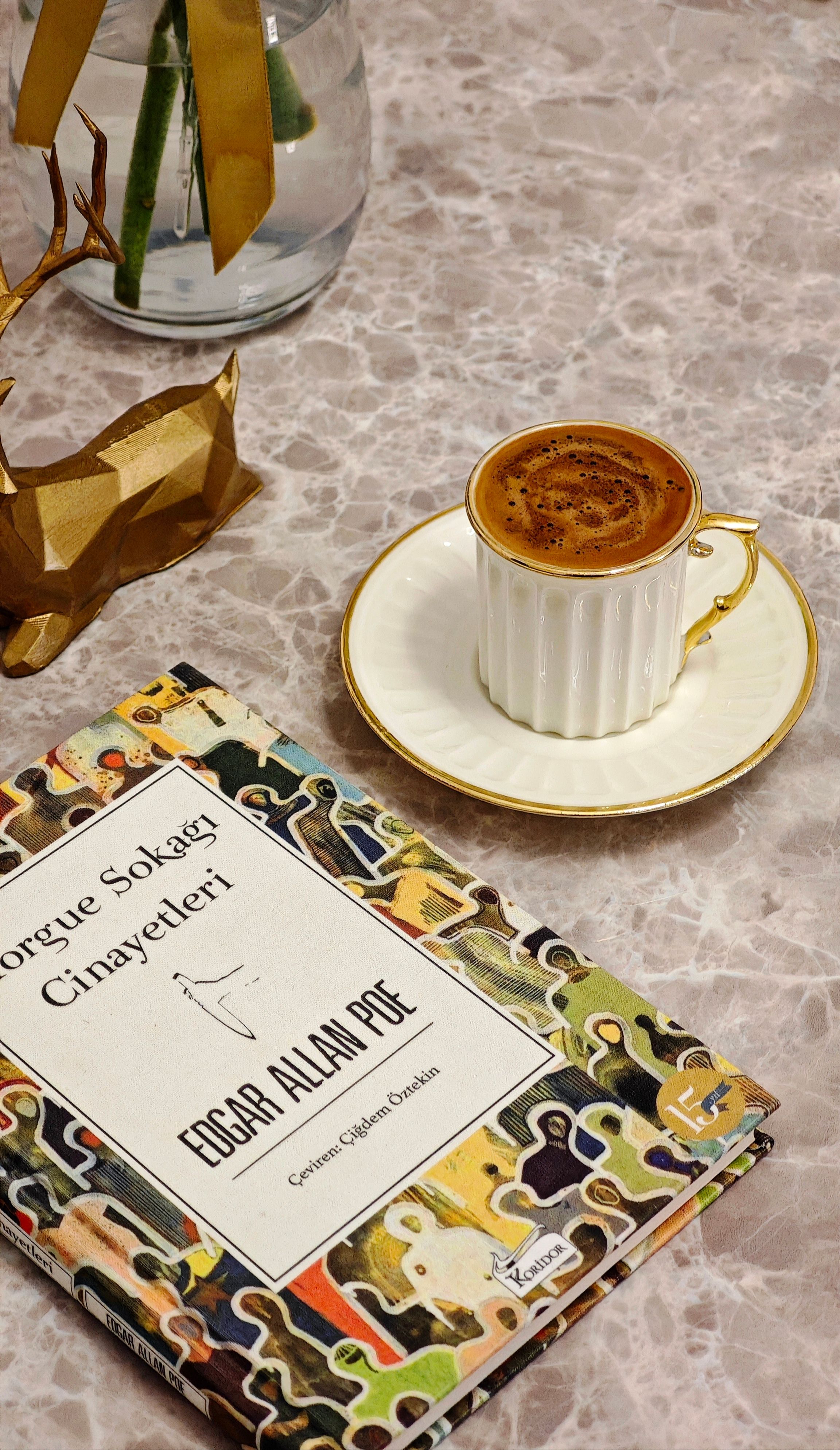 A warm scene featuring a coffee cup beside an Edgar Allan Poe book on a marble table.