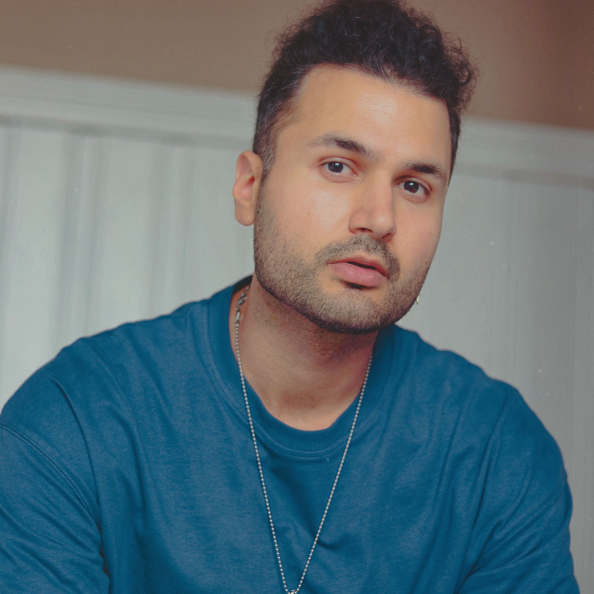 Close-up portrait of a man in a blue shirt with a neutral expression indoors.