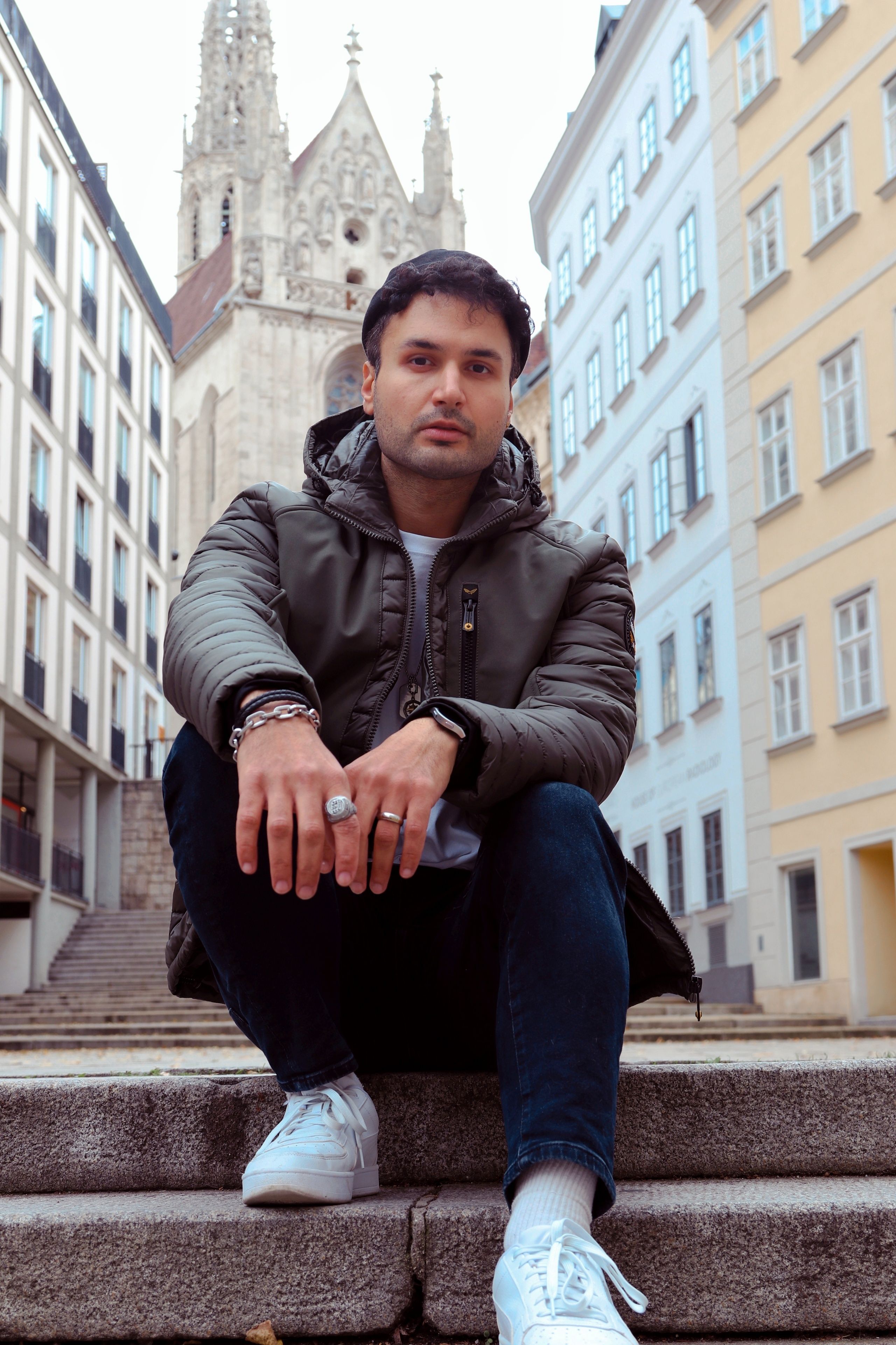A man sitting on urban steps in front of a historic building, exuding a casual and contemplative vibe.