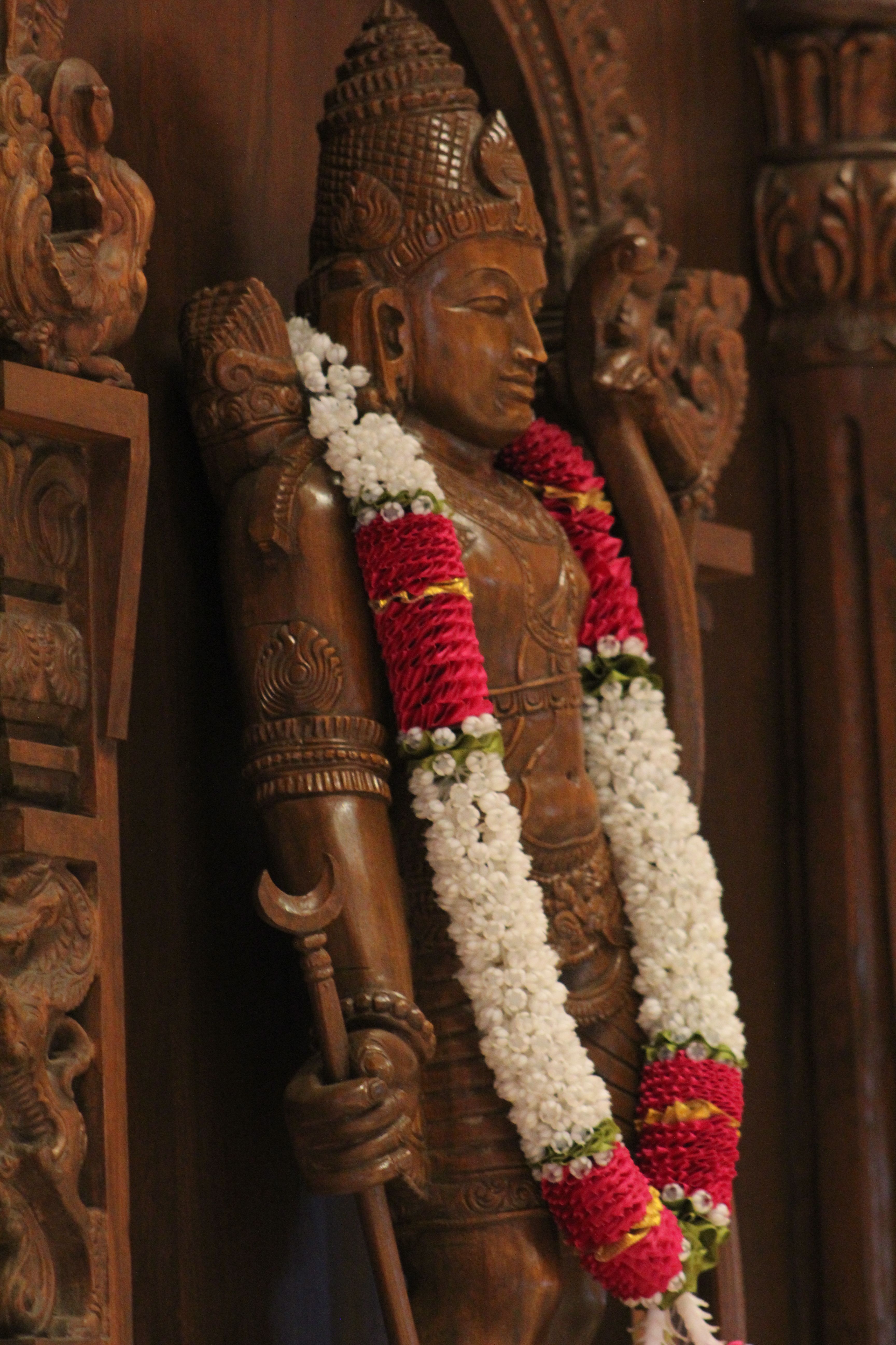Detailed wooden statue with vibrant flower garland in a temple setting.