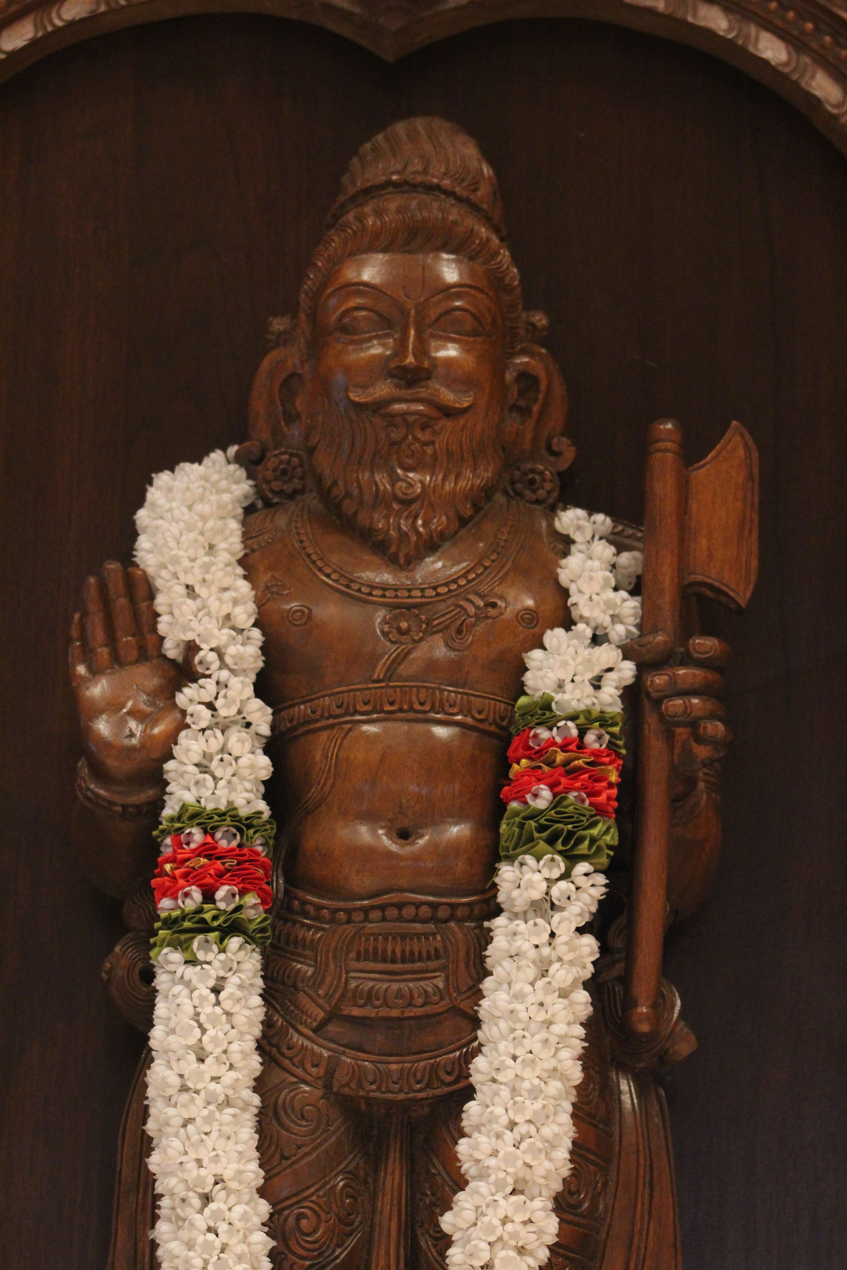 Intricate wooden sculpture of a Hindu deity adorned with floral garlands, showcasing cultural artistry.
