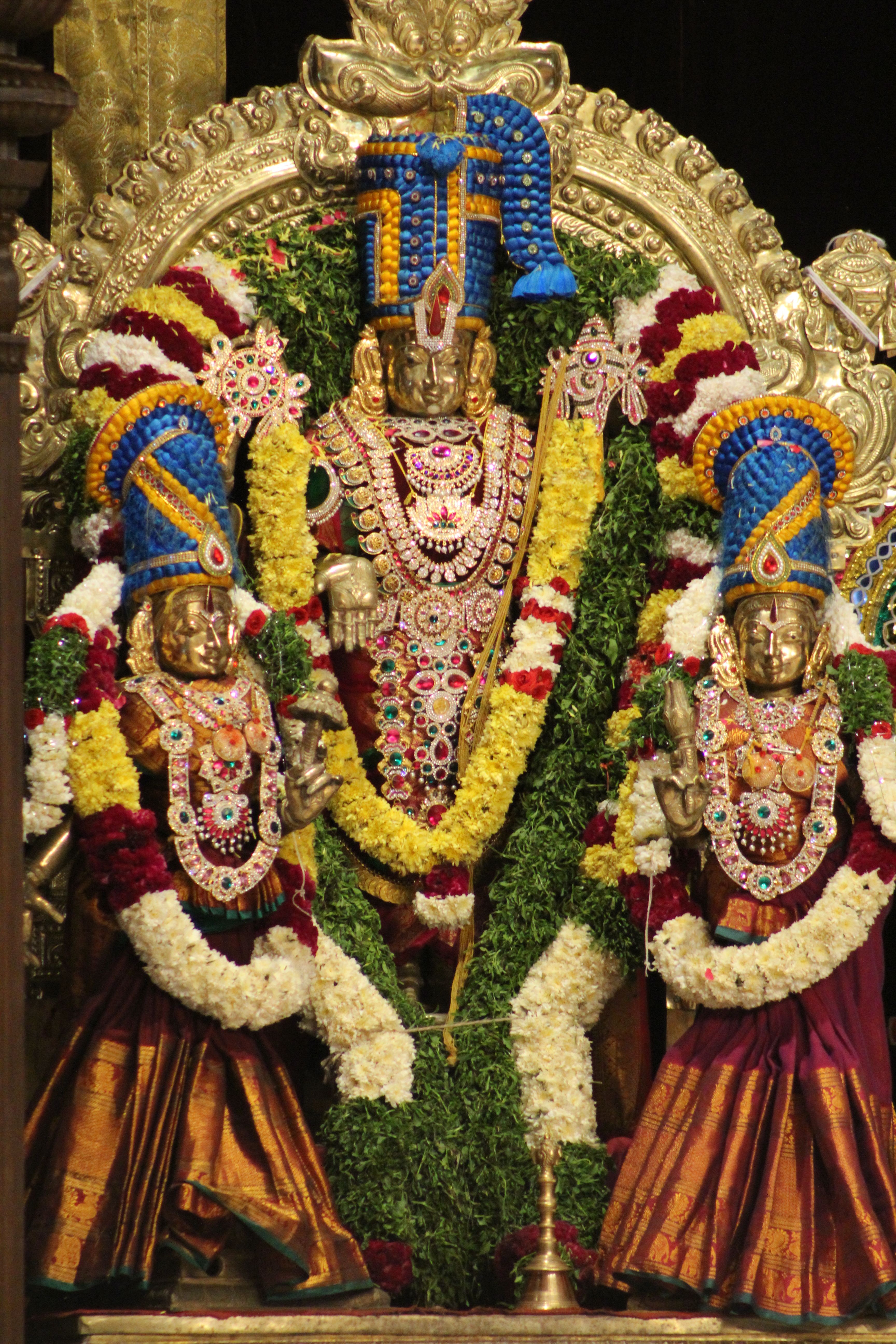 Colorful Hindu deities adorned with flowers and jewelry in a temple setting.