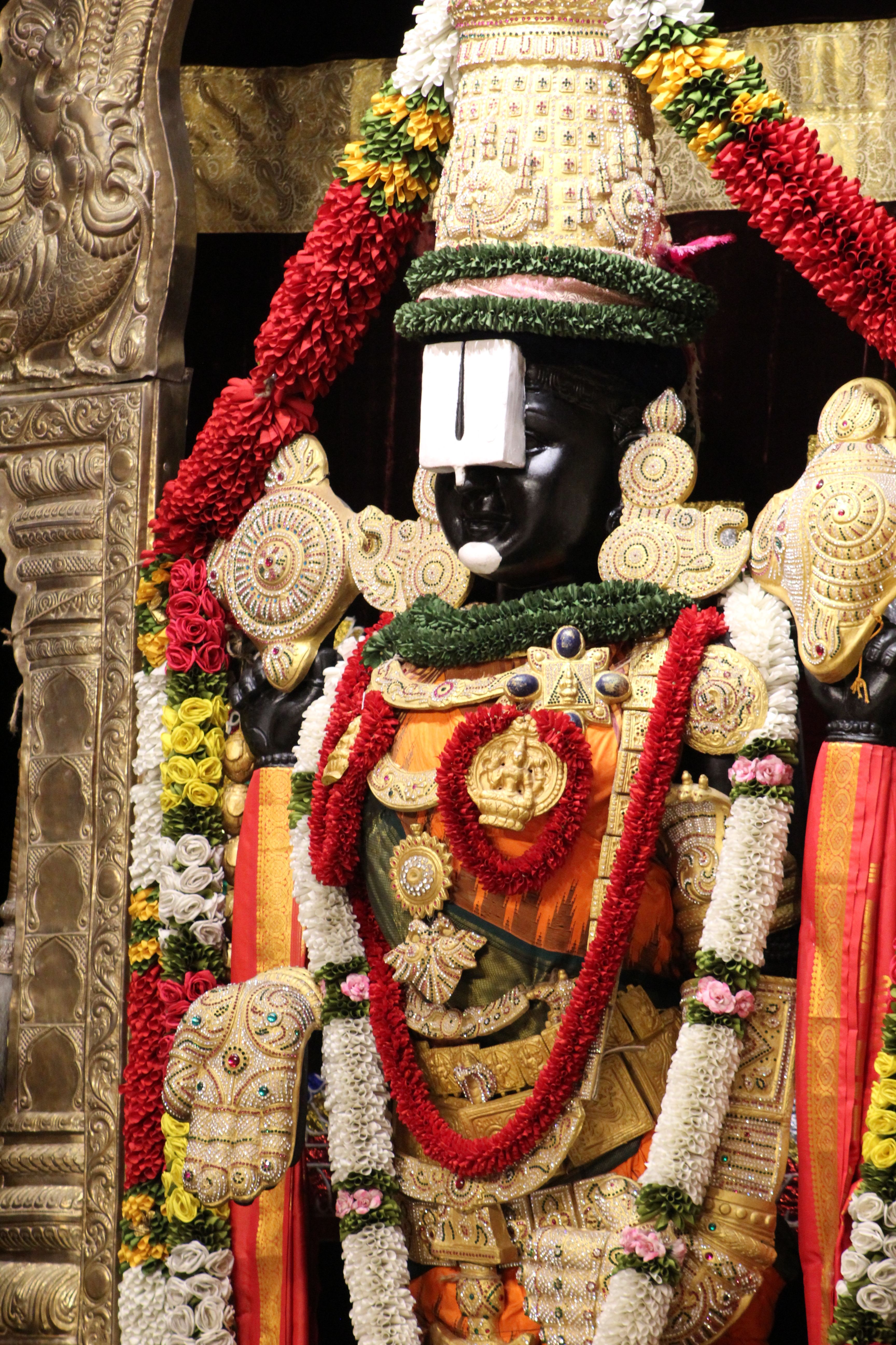 Intricately adorned statue of a Hindu deity with vibrant floral garlands and ornaments.