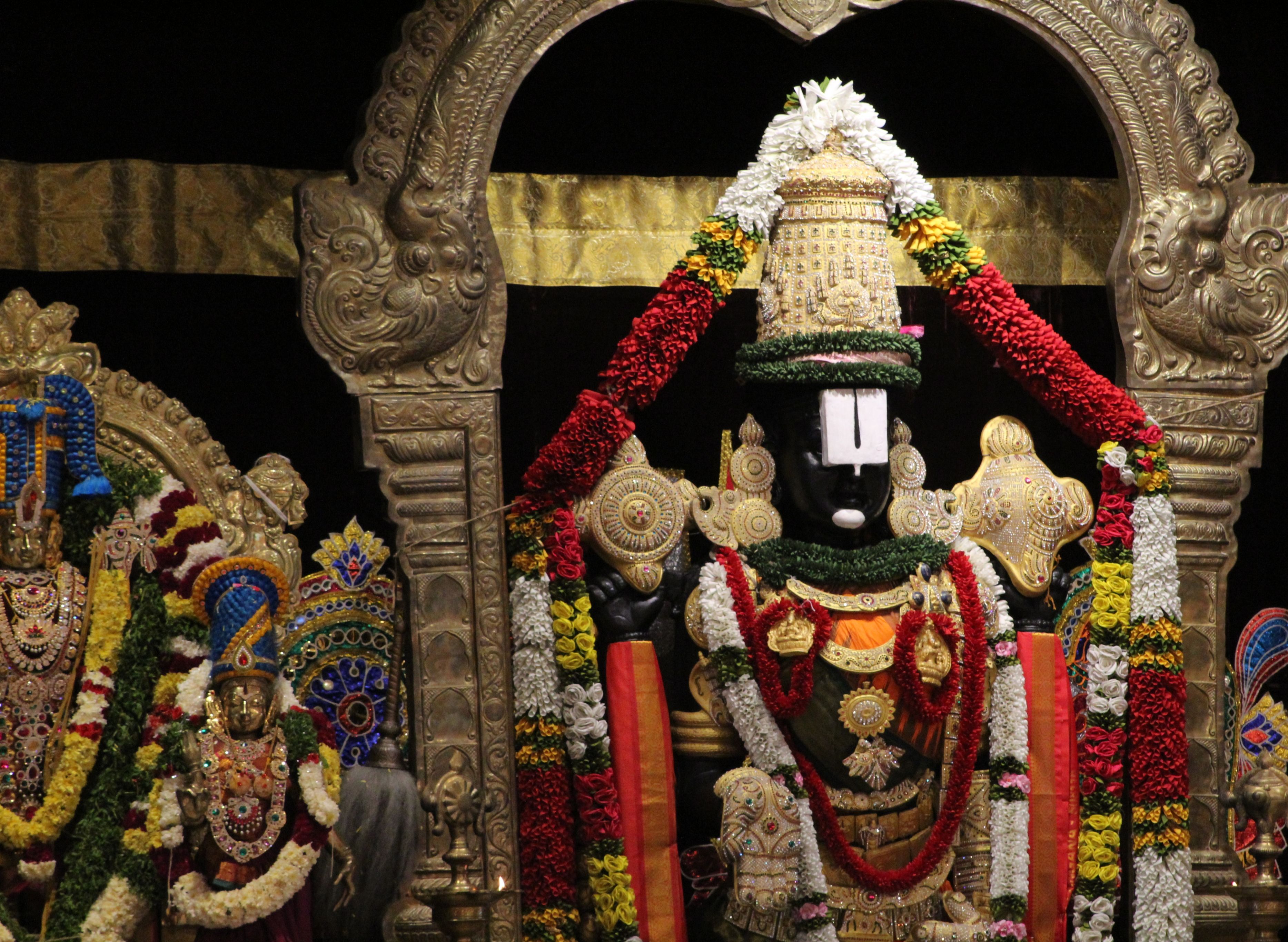 Vibrant Hindu temple decor featuring ornate deity statues adorned with garlands.
