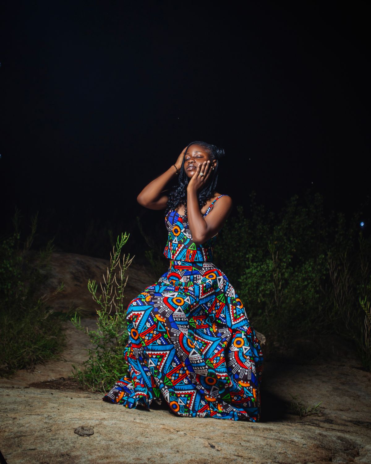 Woman in a colourful African print dress posing outdoors at night