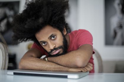 Young man with afro hairstyle resting on a laptop in a home office setting, embodying remote work fatigue — photo by Andrea Piacquadio on Pexels