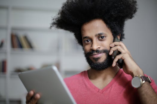 Young confident businessman talking on phone while holding a tablet in a modern office.
