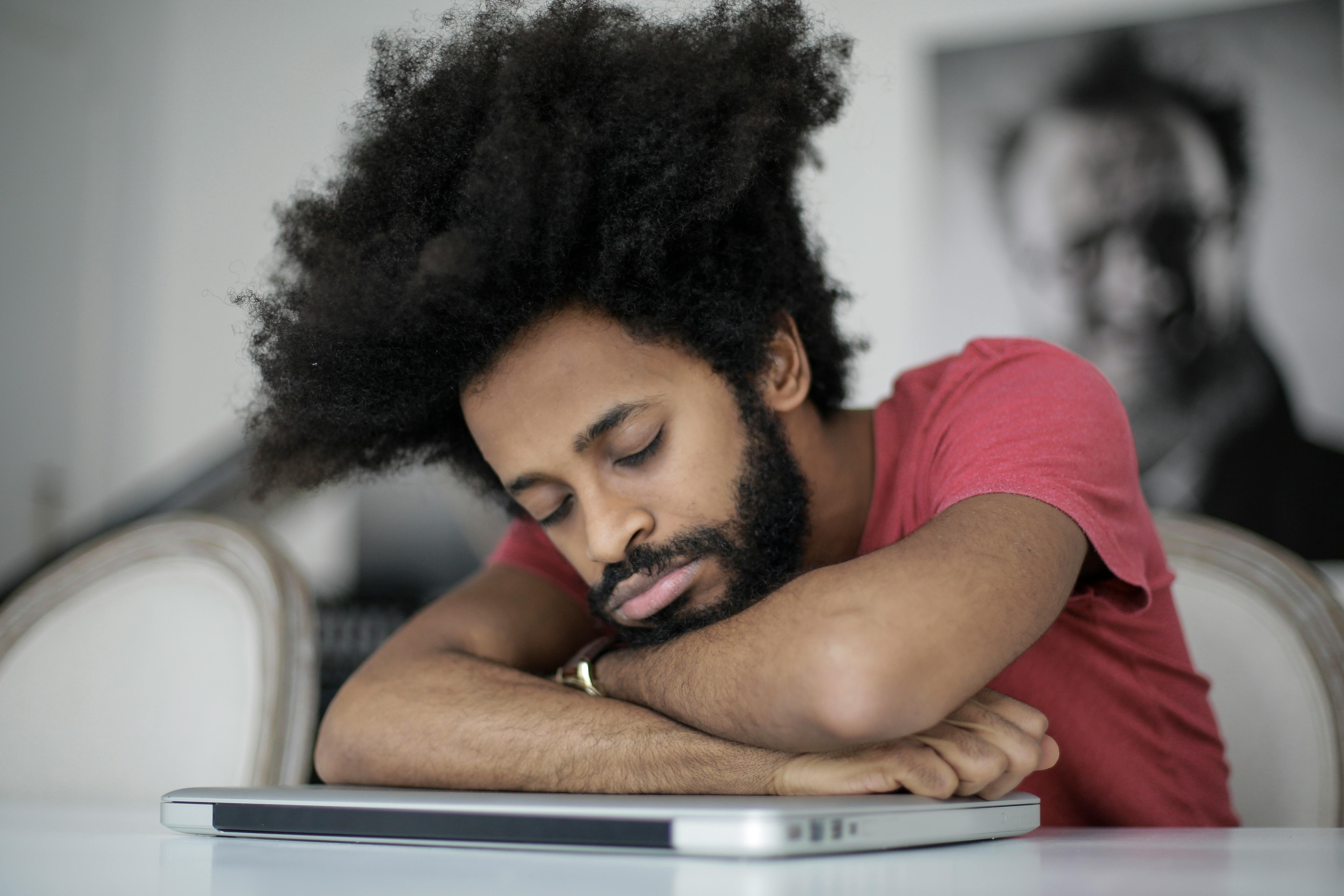 Man with afro hair sleeping on laptop, symbolizing remote work fatigue.