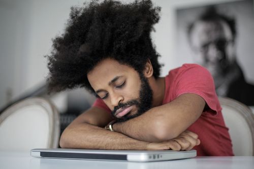 Free Man with afro hair sleeping on laptop, symbolizing remote work fatigue. Stock Photo