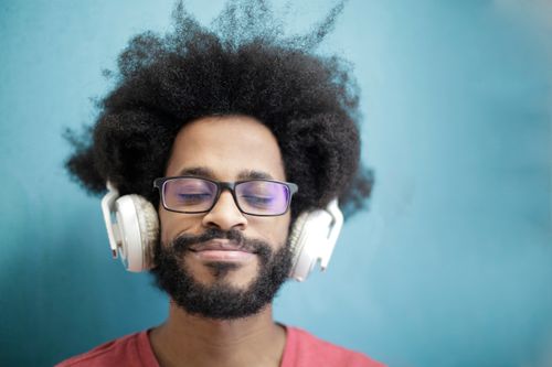 Free A joyful man with afro hair enjoying music with headphones, eyes closed, and a smile. Stock Photo