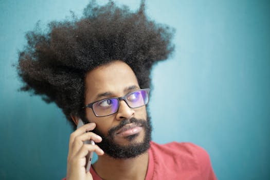 Young man with afro hair making a phone call indoors against a blue background.