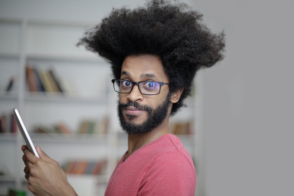 Portrait of a man with afro hair and glasses, using a tablet in a cozy indoor setting. Portrait of a man with afro hair and glasses, using a tablet in a cozy indoor setting.