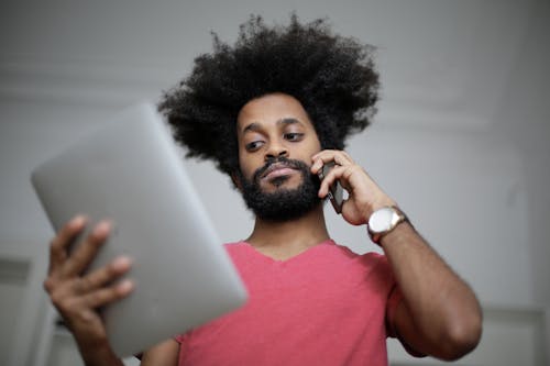 Free Man in Red Crew Neck T-shirt Looking on His Tablet and Making a Call Stock Photo