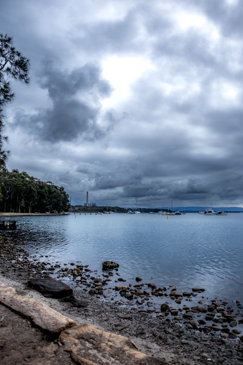 Free A peaceful lakeside scene with a rocky shore and dramatic cloudy sky. Stock Photo