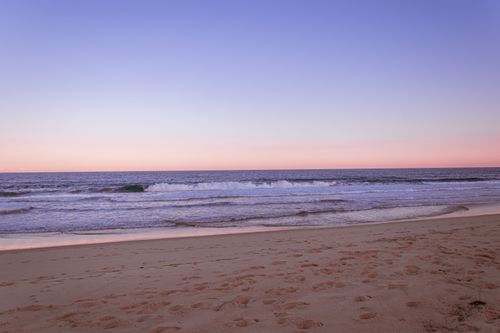 Free A tranquil beach scene with gentle waves under a pastel sunset sky. Stock Photo