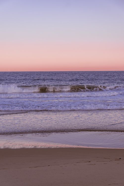 Free Calm waves rolling onto the shore at sunset, featuring pink and purple hues. Stock Photo