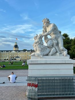 Marble statue with lion near Karlsruhe Palace, blue sky day.