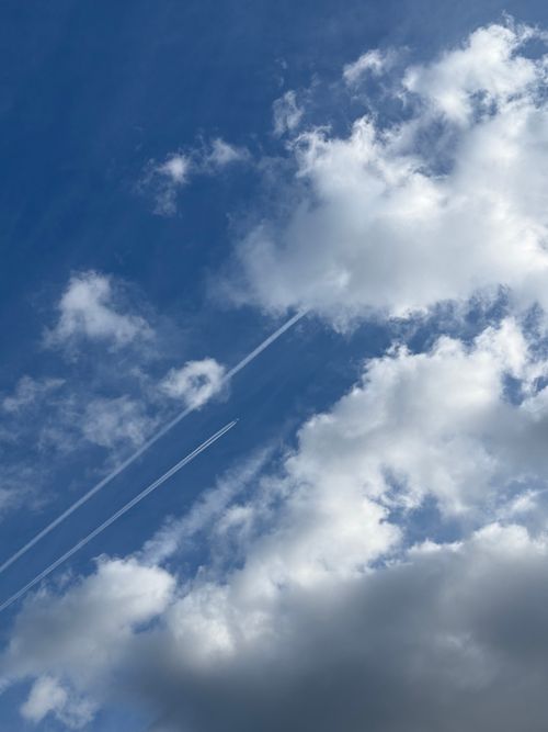 Free A vivid blue sky with clouds and airplane contrails creating dynamic patterns. Stock Photo