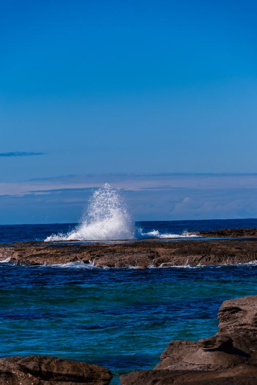 Free Majestic ocean wave crashing against a rocky shore under a clear blue sky, capturing nature's power. Stock Photo