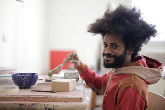 Portrait of a smiling artist with afro hair engaging in arts and crafts in a vibrant indoor setting.