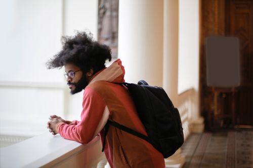 Free A young man with afro hair and a backpack leans on a baluster in an indoor corridor. Stock Photo