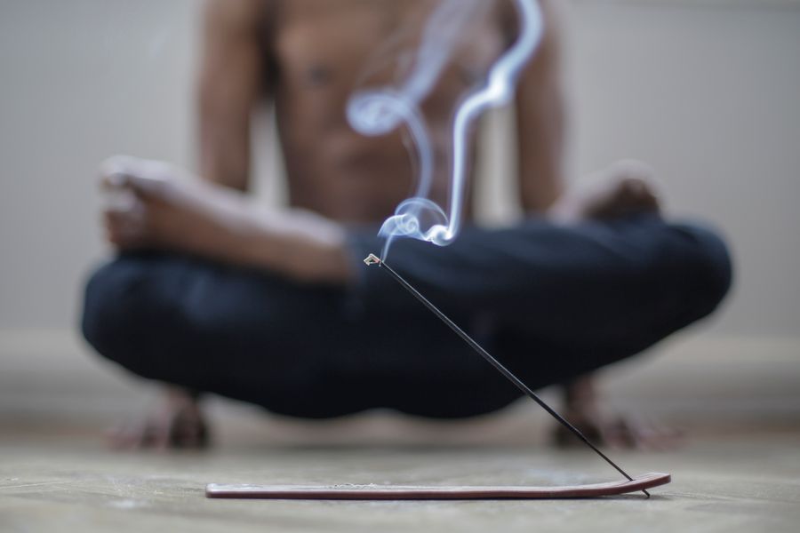 Silhouette of a person meditating in low light with drifting incense smoke