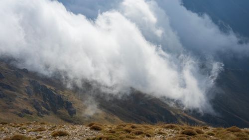 Free Clouds rolling over a rugged mountain landscape create a dramatic and atmospheric scene. Stock Photo