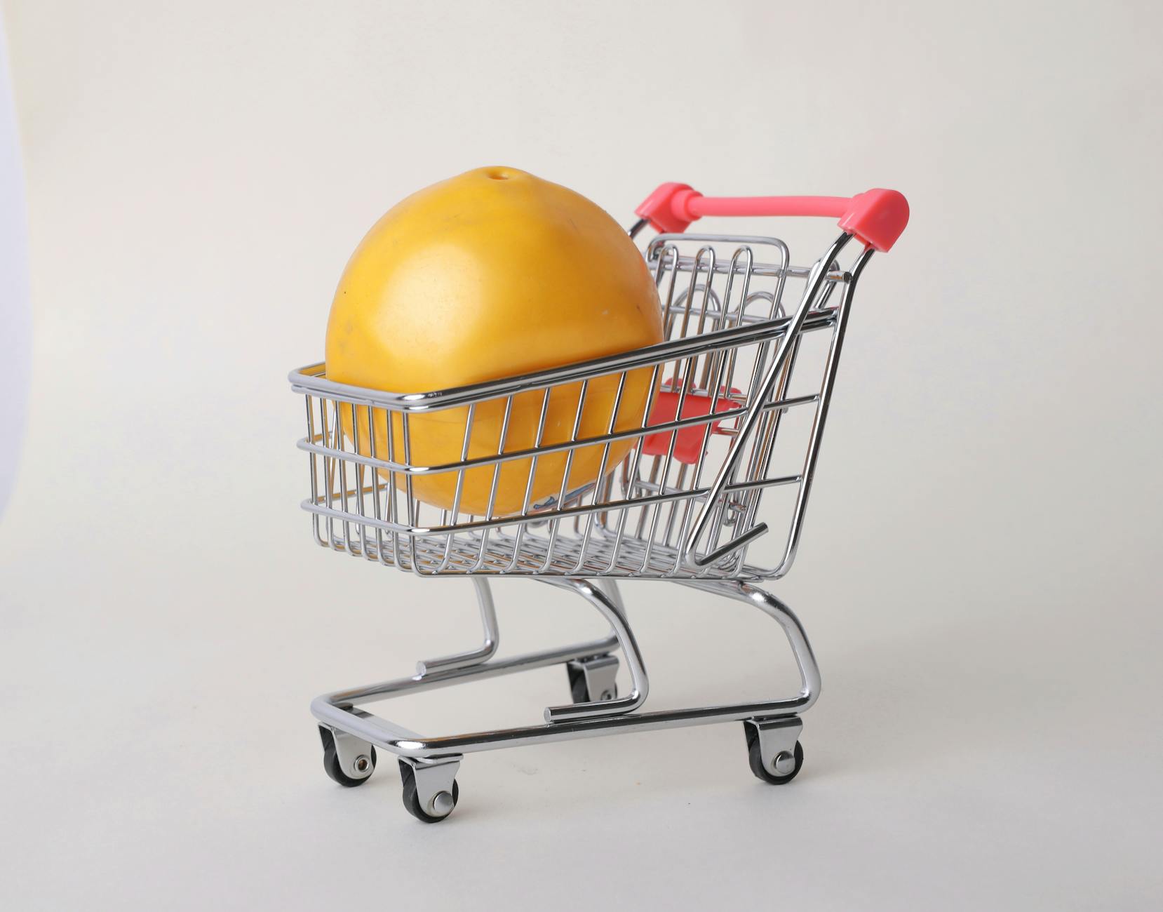 A minimalistic studio shot of a mini shopping cart containing a large yellow fruit.