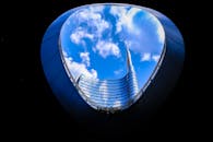 透过圆形建筑框架，可以看到一座现代摩天大楼反射着云层