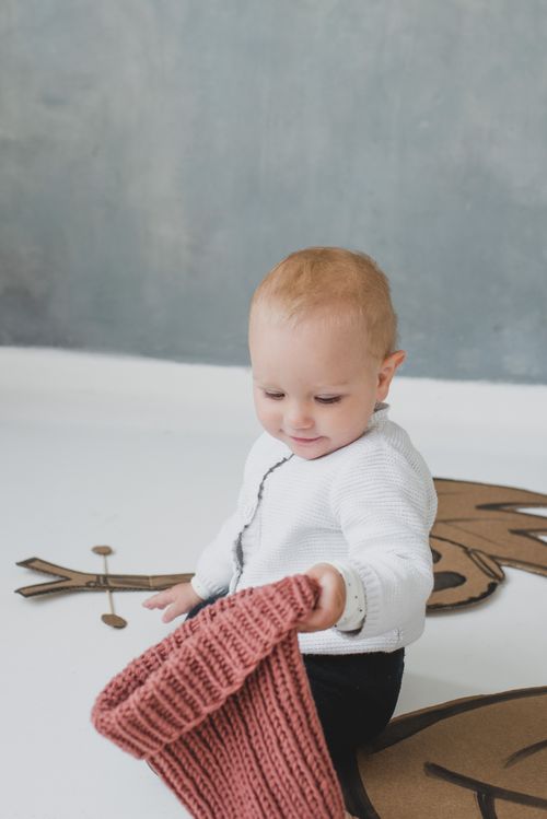 Free Cute toddler exploring a knitted beanie while sitting on a stylized floor design. Indoor setting. Stock Photo
