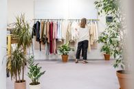 一名妇女正在一家精品店里浏览衣服，店内摆满了室内植物和时尚陈列品，营造出理想的时尚零售场景