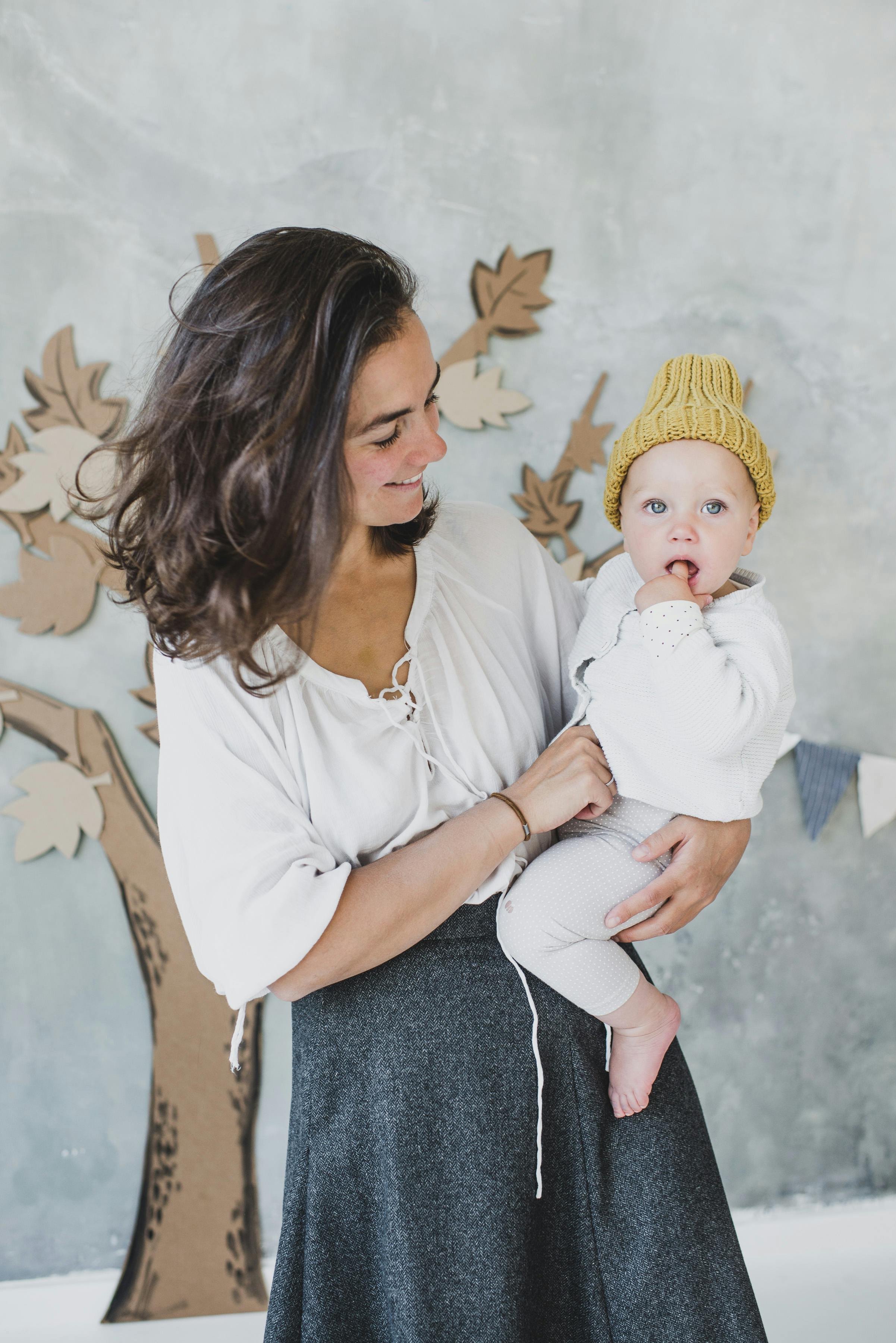 woman in white top carrying a child in a knitted beanie