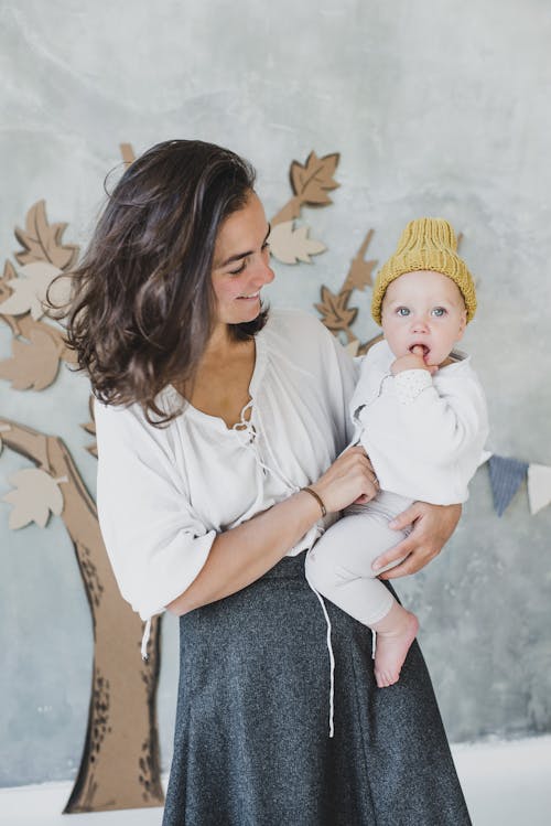 Free Woman in White Top Carrying a Child in a Knitted Beanie  Stock Photo