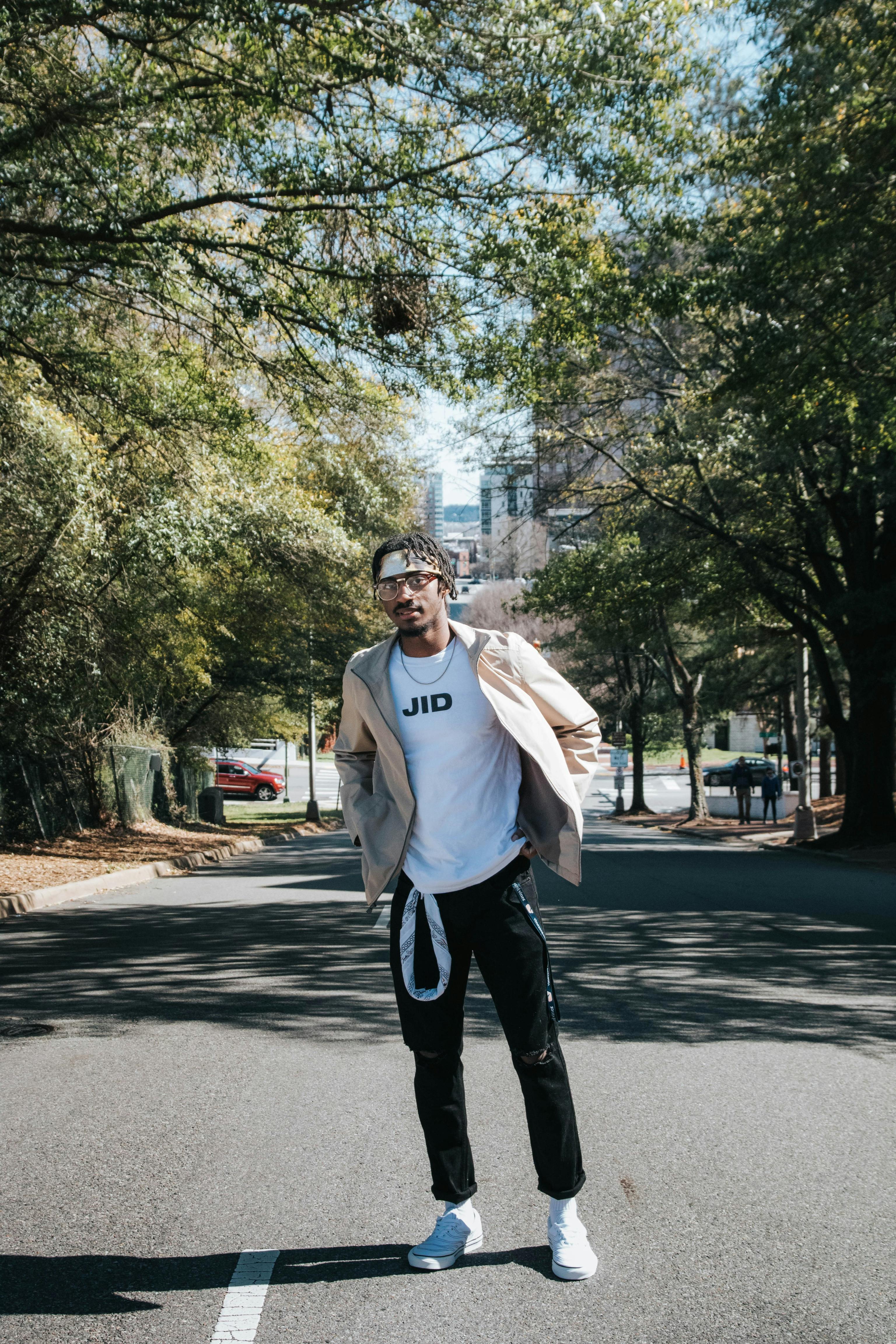 Young adult man posing stylishly on a tree-lined street in urban setting.
