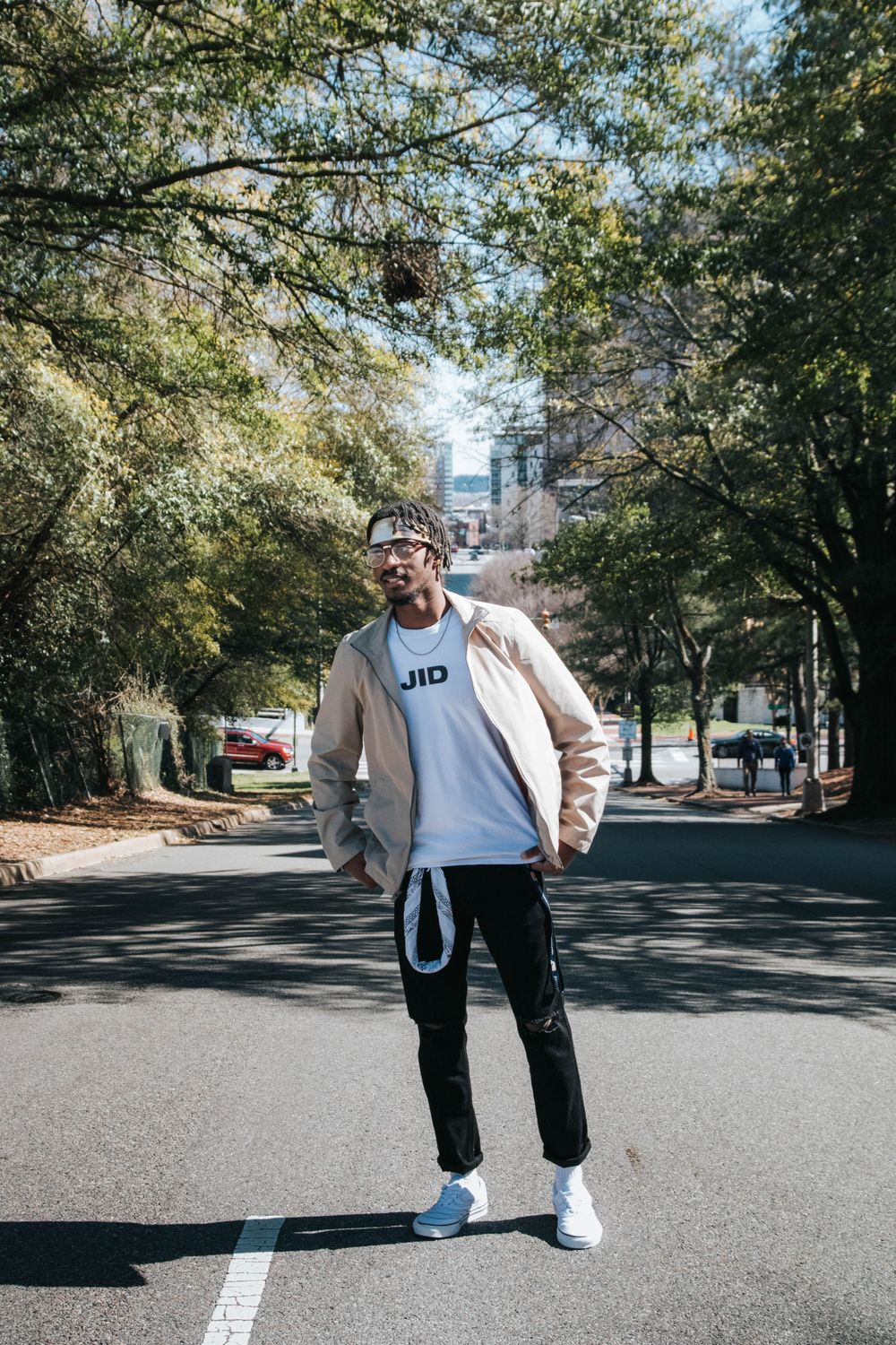 Man wearing a beige jacket, dark trousers, and sunglasses on a city street