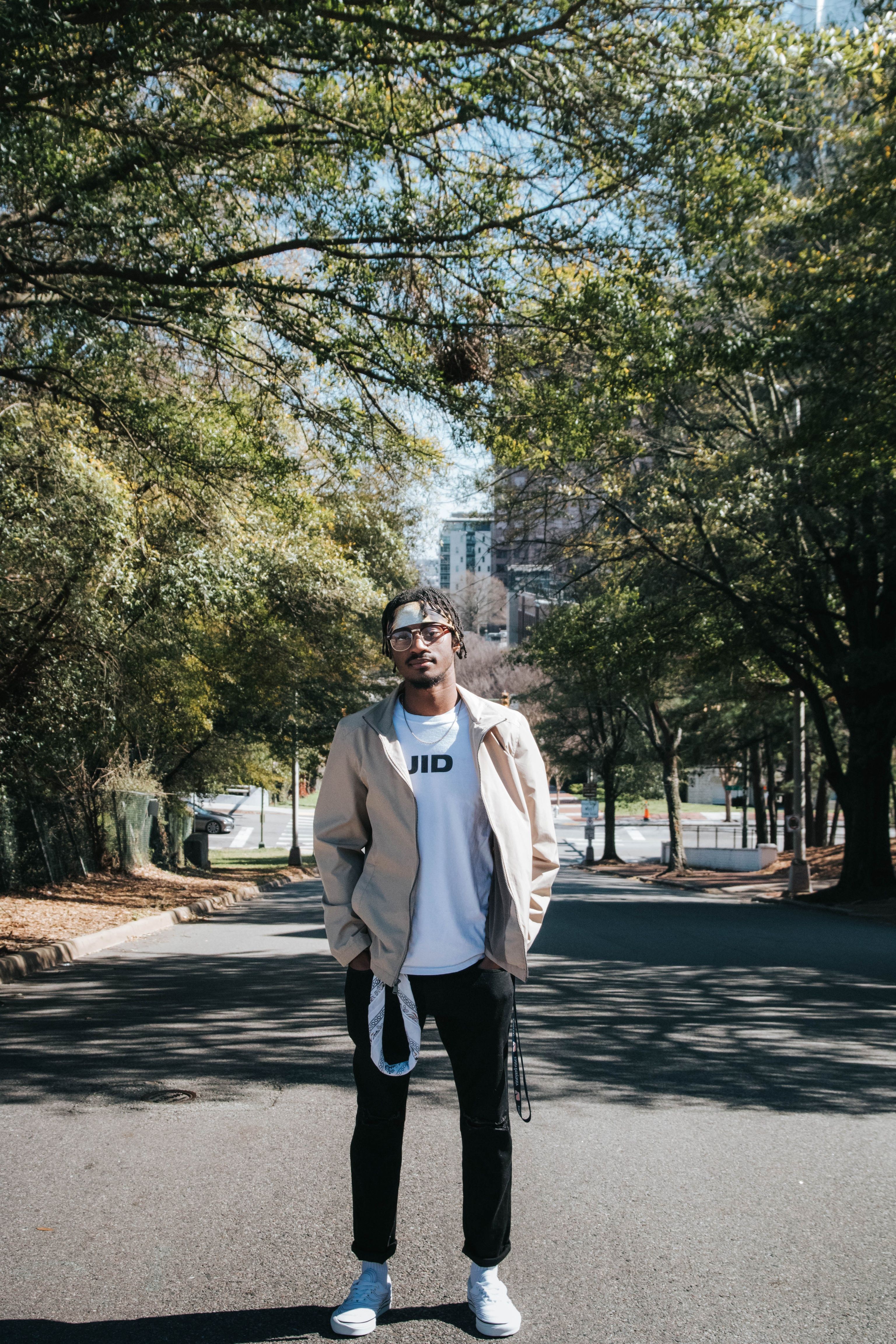 Young adult in casual attire standing on a city street surrounded by trees.