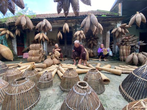 Free Elderly artisans crafting traditional bamboo baskets in an outdoor setting, surrounded by handcrafted woven items. Stock Photo