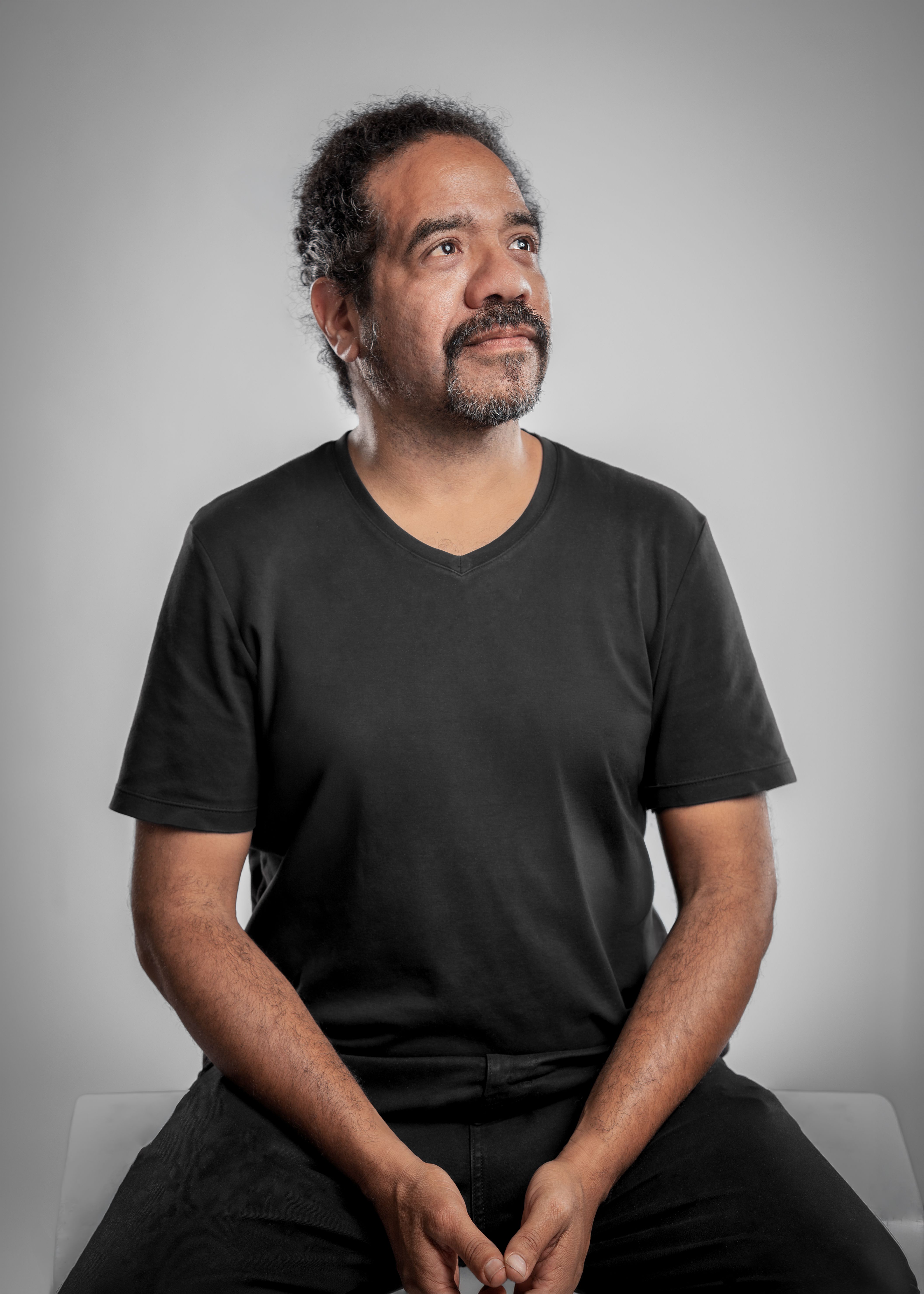 Reflective middle-aged man in casual attire looking upwards in a studio setting.