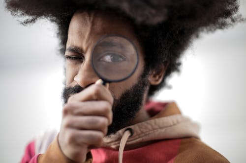 Person in Red and Brown Jacket Holding Magnifying Glass