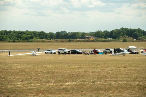 Free A rural airfield scene with a small gathering of people, cars, and gliders on a sunny day. Stock Photo