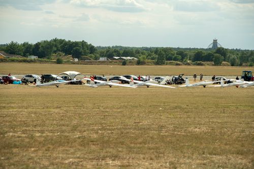 Free A row of glider aircraft and cars parked on a grassy airfield with people around. Stock Photo