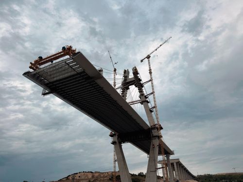Free A modern bridge under construction with cranes and cloudy sky backdrop. Stock Photo