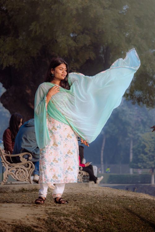 Free A woman in traditional attire enjoys a breezy day outdoors, draped in a flowing turquoise scarf. Stock Photo